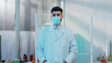 Kameranın önünde kimya laboratuvarında bilim adamı pozu veren koruyucu maske takmış ve doğrudan kameraya bakıyordu.