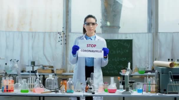 Mulher cientista bonita no laboratório bioquímico segurando um cartaz com o conceito Stop Coronavirus de uma pandemia Covid-19 — Vídeo de Stock