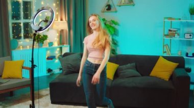 Sosyal medya hesabı için güzel bir video hazırlayan mutlu bir kadın evde otururken akıllı telefon ve ışık halkası kullanarak video kaydediyor.
