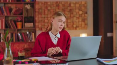 Çevrimiçi öğrenci ödevi laptopla diğer öğrenciler ve öğretmenlerle konuşuyor. Karizmatik sarışın bayan kameranın önünde oturuyor.