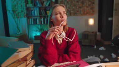 Karizmatik bir genç kadın, evde düşünen bir yüzle üniversite projesini yapıyor gözlüklerini alıyor ve işini düşünüyor.