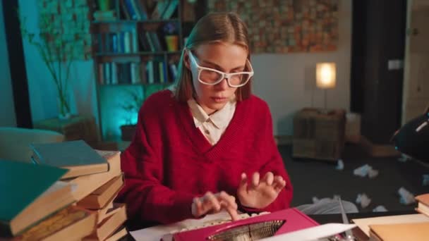 Denkende Dame mit Brille tippt einige Dokumente auf die Schreibmaschine in der Bibliothek, in der sie ihr Geschichtsprojekt beendet — Stockvideo