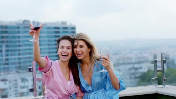 Excited and attractive two best friends ladies in pajamas on the roof top of loft apartment holding glasses of wine and enjoying the evening time — Stock Video