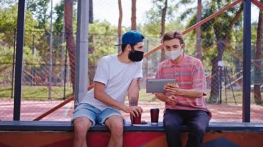 In the quarantine two guys studying together in the park at fresh air they using a electronic tablet to analyzing some documents then continue to discussing concept of Coronavirus