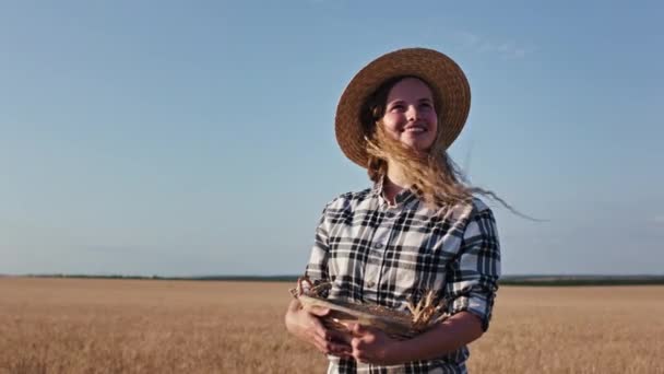 Farmer lady countryside in front of the camera in the middle of a large wheat field holding a basket of a wheat grass and looking to the sun feeling happy — Stock Video