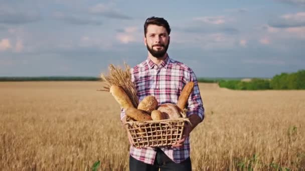 黄金の小麦畑の真ん中に立っている有名な男の肖像画手に新鮮なパンの箱を持っている — ストック動画