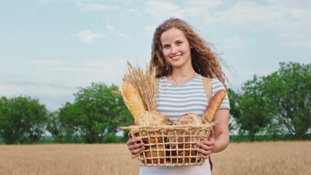 Kameranın önünde uzun kıvırcık saçlı, buğday tarlasının ortasında içi taze ekmek dolu bir kutuyla çekici bir bayan. — Stok video