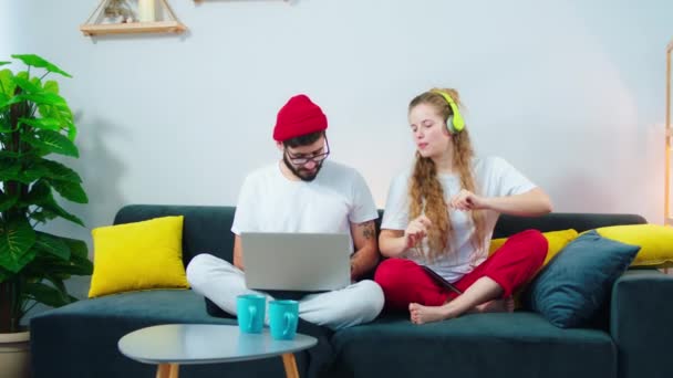 Ballando e cantando donna emotiva a casa mentre ascoltava musica dalle cuffie il suo uomo fidanzato che usa il computer portatile per lavorare — Video Stock