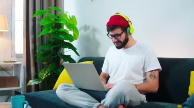 Hevesli genç erkek öğrenci evde online kursuna gidiyor dizüstü bilgisayarında bir proje yazıyor ve kulaklıklardan müzik dinliyor.