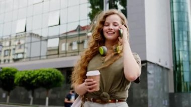 Caddenin aşağısında uzun saçlı kadın akıllı telefonuyla konuşuyor ve rüzgarlı bir günde kahve içiyor. 4k