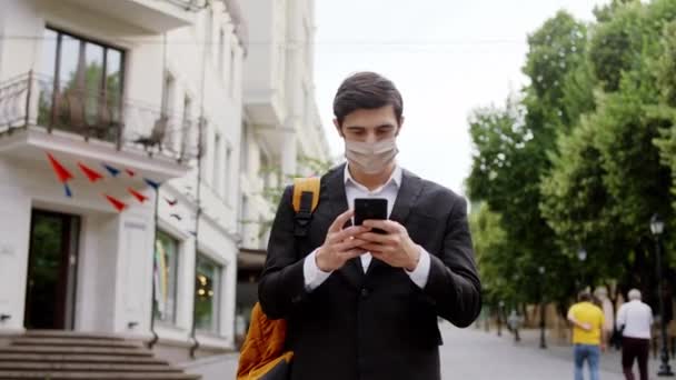 In the middle of the street businessman walking down on the street typing something on smartphone he wearing protective mask Covid-19 — Stock Video