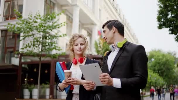 Zeer charismatische man en goed uitziende vrouw twee studenten nadat ze cursus wandelen en bespreken iets met behulp van de digitale tablet in het midden van de straat. 4k — Stockvideo