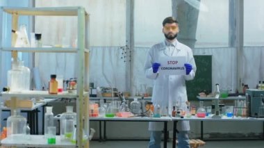 Retro kimya laboratuvarında çalışan bilim adamı kameraya doğru odaklanmış ve elinde Stop Coronavirus 'un olduğu bir poster tutuyordu.