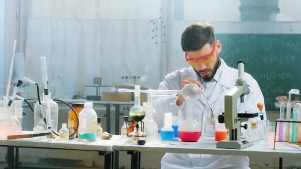 W biochemicznym laboratorium naukowiec używający jakiegoś płynu chemicznego, by dodać reakcję chemiczną do szklanych zbiorników. Strzał na ARRI Alexa Mini. — Wideo stockowe