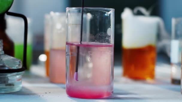 Vóór de camera een close-up maken van een roze chemische stof gemengd op de kolf in het chemisch laboratorium — Stockvideo