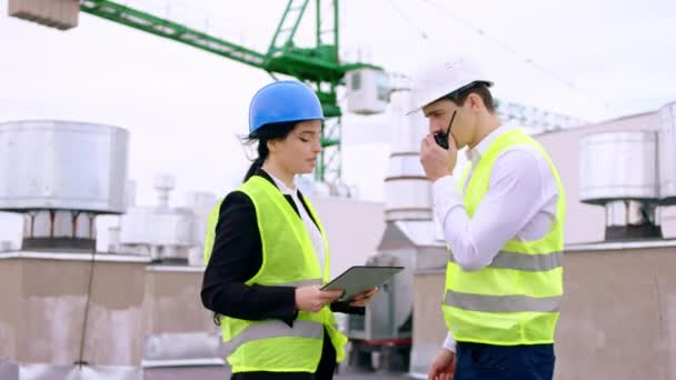 Assistente carismática e empresária no telhado do canteiro de obras discutindo sobre o plano de golpe que eles usam um homem tablet digital levar as telecomunicações de rádio para falar com — Vídeo de Stock