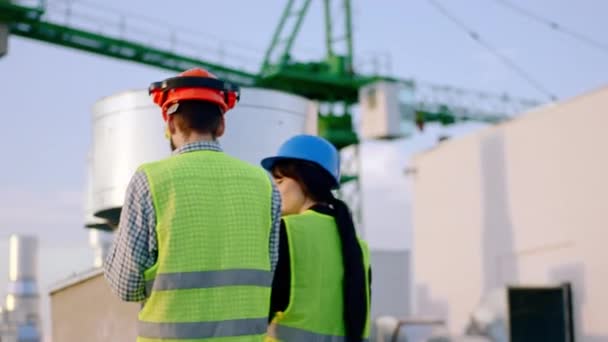 Wandelen door de top van de bouwplaats twee ingenieurs dame en man dragen veiligheidshelmen ze hebben een bespreking samen — Stockvideo