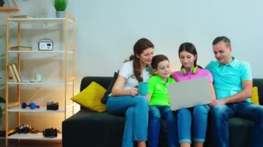 İyi görünümlü bir aile birlikte oturma odasında vakit geçirir kanepede oturur ve dizüstü bilgisayarda film izlerler.