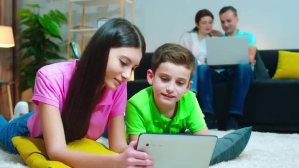 Em casa no soma pais felizes usando laptop para assistir algo juntos, enquanto as crianças usando tablet para jogar alguns jogos — Vídeo de Stock