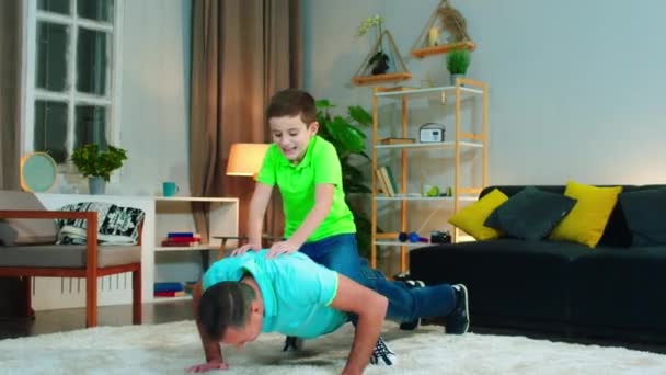 Usmívající se a vzrušený chlapeček se baví se svým tátou, dělají kliky v obýváku, malý chlapec je přes jeho tatínky zpět. Zastřelen na ARRI Alexa — Stock video