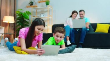 Evde soma mutlu ebeveynler birlikte bir şeyler izlemek için dizüstü bilgisayar kullanırken çocuklar bazı oyunlar oynamak için tablet kullanıyorlar.