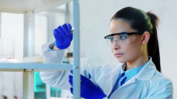 Cientista mulher carismática close-up para a câmera tomar um conta-gotas e adicionar algum líquido químico na banheira de vidro no laboratório de química — Vídeo de Stock