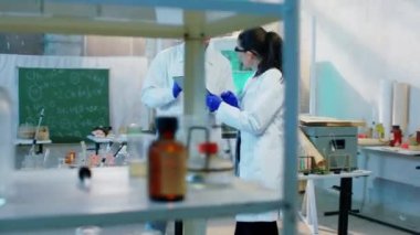 Eczacı kadın ve asistanları kadın ve erkek, kimyasal maddeyle birlikte çalışarak dijital tablete kimyasal reaksiyon sonucu yazdılar. 4k