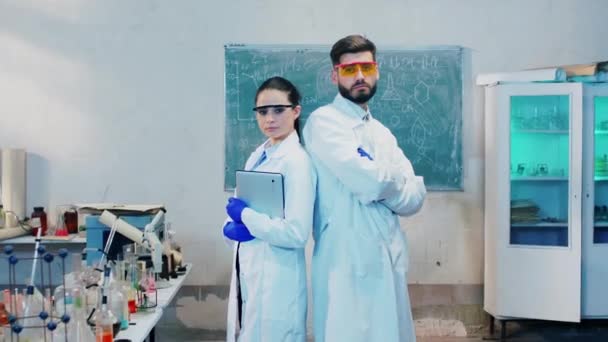 Posing allvarliga två farmaceut man och kvinna tittar rakt in i kameran i farmaceutiskt labb de har korsning händer — Stockvideo