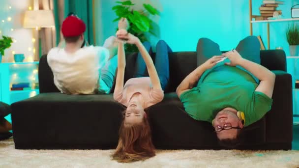 Młodzi zabawni przyjaciele wielonarodowe robi ćwiczenia podczas pobytu w domu na kanapie robią chrupki schudnąć — Wideo stockowe