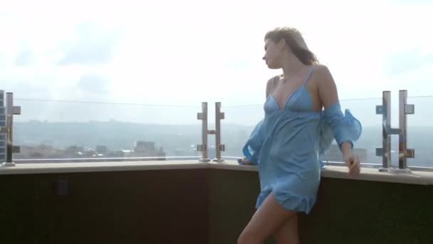 Giorno ventoso signora romantica carismatica in un pigiama blu godendo il tempo sul tetto del suo appartamento. Girato su ARRI Alexa — Video Stock