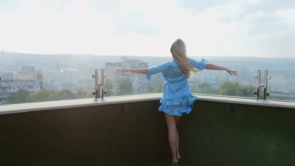 Утром на крыше мансардной квартиры симпатичная дама в синей пижаме наслаждается временем, которое она чувствует себя расслабленной и счастливой, глядя в камеру и улыбаясь — стоковое видео