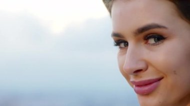 Mükemmel beyaz gülüşü olan güzel bir kadının portresi doğrudan kameraya bakıyor ve rüzgarlı bir günde heyecanlanıyor. 4k