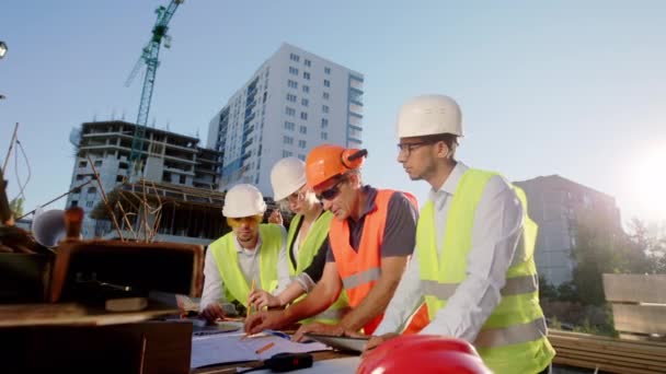 Grande equipe do canteiro de obras de engenheiros e arquitetos todos juntos trabalhando no plano de construção a discussão concentrada entre si — Vídeo de Stock