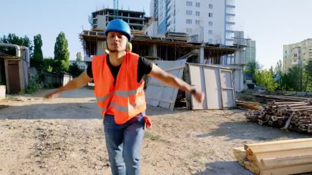 Auf der Baustelle vor der Kamera tanzte ein junger afroamerikanischer Bauarbeiter vor der Kamera und hörte in der Pause Musik aus den Kopfhörern. — Stockvideo