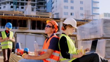 Foreman orta yaşlı ve ekibi inşaat alanında mola veriyor. Yemek yiyor ve tatilin tadını çıkarıyorlar. Güvenlik ekipmanları giyiyorlar.