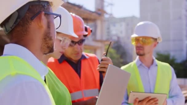 Em frente ao grupo de câmeras de diversos especialistas idosos e multiétnicos analisando o plano de canteiro de obras eles vestem equipamentos de proteção — Vídeo de Stock