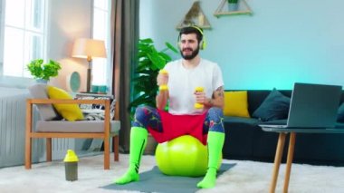 Pazıları üzerinde çalışan bir adam kendinden çok memnun, sarı ağırlıkları kullanarak ve bir topun üzerinde çalışırken çok fazla gülümsüyor.