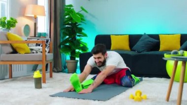 Adam paspasının üzerinde halıda oturuyor, iki bacağını da esnetiyor ve güzel spor kıyafetleri giyiyor, yaralı görünüyor. ARRI Alexa 'da çekim