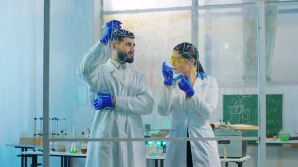 Mujer guapa y su colega científico escriben juntos la fórmula química en la placa transparente en el laboratorio de química. Disparo en ARRI Alexa Mini. — Vídeos de Stock