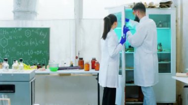 Bir retro laboratuarında iki ilaç uzmanı birlikte çalışarak kimyasal reaksiyon testinin sonuçlarını analiz eder ve birlikte tartışırlar. ARRI Alexa Mini 'de çekilen.
