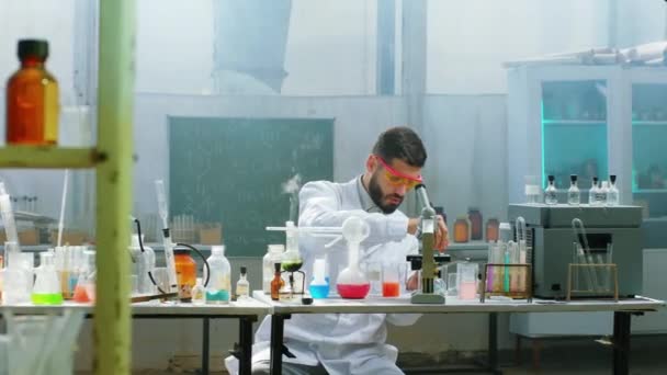 Bonito cientista homem usando um conta-gotas para adicionar no tubo de vidro ele se concentrou trabalhando no laboratório de química vestindo uniforme protetor — Vídeo de Stock