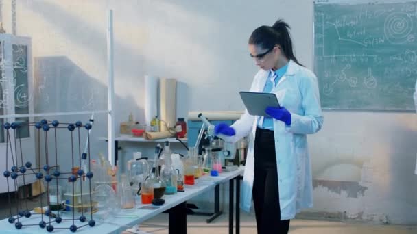 Im biochemischen Labor Gruppe von Wissenschaftlern mit digitaler Tablette und Tafel, um einige chemische Formel zu schreiben, um das Ergebnis der Antivirus-Impfstoff-Konzept der pharmazeutischen Industrie zu identifizieren — Stockvideo