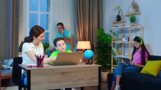 Gyönyörű nagy család a nappaliban szülők segítenek a fiúnak a házi feladatban a laptop segítségével befejezni a munkát — Stock videók