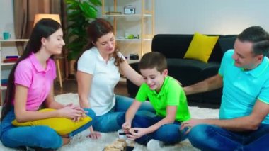 Oturma odasında, yerde büyük mutlu bir aile birlikte vakit geçiriyorlar. Tahta bloklar oyununda oynuyorlar ve anın tadını çıkarıyorlar.