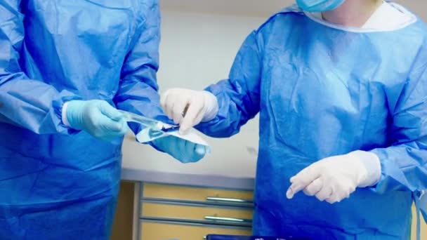 Dois médicos na clínica vestindo equipamentos de proteção se preparam para iniciar uma operação cirúrgica — Vídeo de Stock