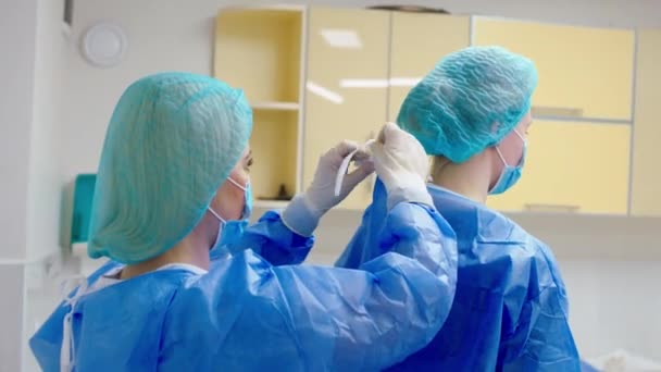 A klinikán, mielőtt elkezdené a műtétet a női nővér segít öltözködni, hogy az orvos speciális védőfelszereléssel. Lelőtték az ARRI Alexán. — Stock videók