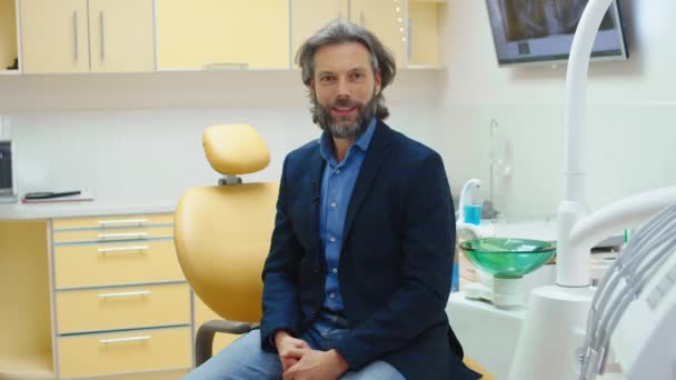 Charismatický dobře vypadající muž pacient na zubní klinice se posaďte na židli zubaře poté, co ukončil svou návštěvu zubaře dívá přímo do kamery a dává dobrou zpětnou vazbu — Stock video