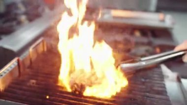 Chef preparing a beef steak in front of the camera on the professional grill he add some more fire to cooked well the steak