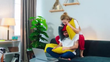Happy with a large smile couple on the sofa in living room playing together funny with pillows on the living room. 4k