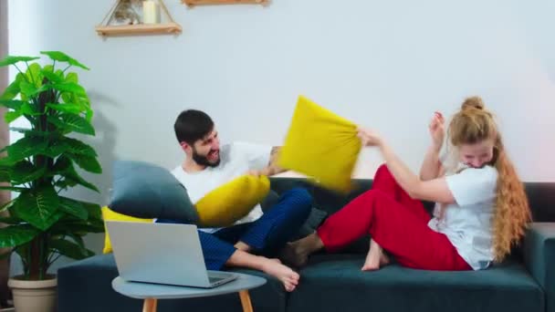 Modern living room battle time between one charismatic couple playing with pillows they smiling large and feeling excited — Stockvideo